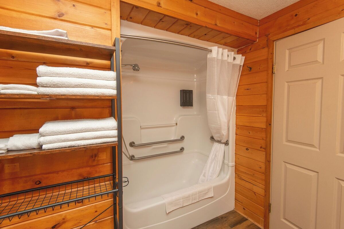 Une salle de bain rustique, avec des murs en bois, une baignoire blanche, un rideau de douche et un porte-serviettes sur lequel sont pliées des serviettes.