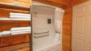 Une salle de bain rustique, avec des murs en bois, une baignoire blanche, un rideau de douche et un porte-serviettes sur lequel sont pliées des serviettes.