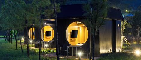 A modern, circular building with a flat roof, surrounded by trees and illuminated by artificial lighting.