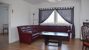 Una habitación con un sofá de cuero, una mesa de comedor, una silla, una lámpara de pie y una ventana con cortinas.