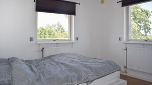 Un dormitorio con cama, dos ventanas, radiador y calefactor de pared.