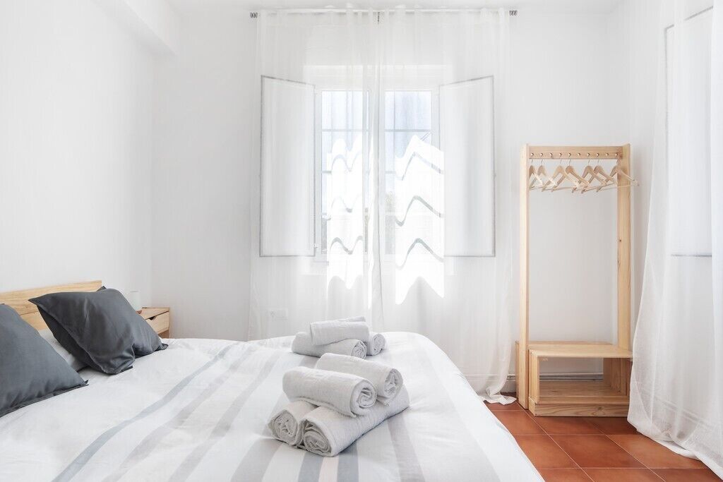 A hotel room with a bed, a wooden bench, and a clothing rack.