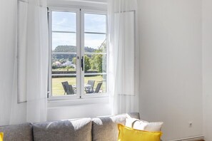 Ein Zimmer mit einem großen Fenster, einem grauen Sofa und einem gelben Kissen.