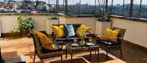 A rooftop terrace with outdoor furniture, a large umbrella, and a view of the cityscape.