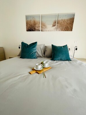 A neatly made bed with a white duvet, two teal pillows, and a wooden tray with two white cups and a green plant. - Modern, renovated apartment with a beautiful panoramic terrace (Roma)