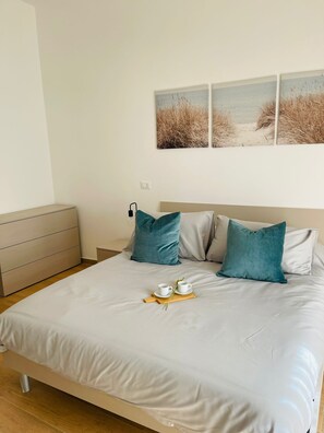 Un letto rifatto con un lenzuolo bianco, due cuscini color acquamarina e un vassoio con una tazza e un libro.