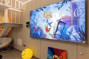 Una pantalla de televisión muestra 'A Tale of Two Cities' con una animación colorida, una silla blanca, un globo amarillo con forma de cara sonriente y un altavoz montado en la pared.