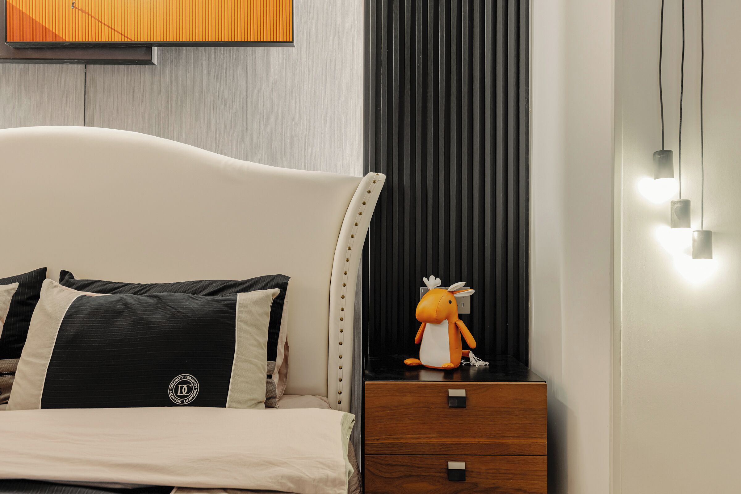 Une chambre à coucher avec un lit, une table de chevet, un jouet en peluche et un luminaire fixé au mur.