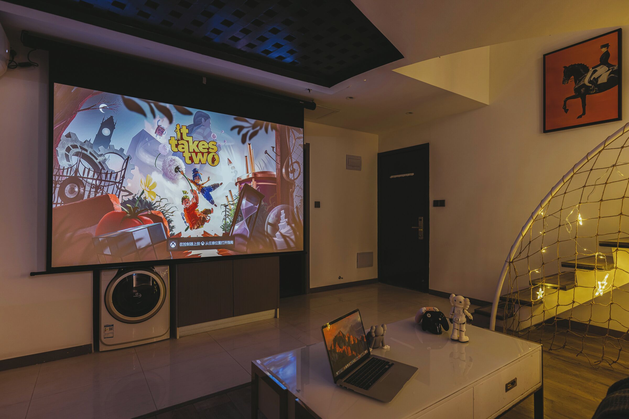 Una stanza con un grande schermo che mostra un videogioco, un portatile e un orsetto da tavolo.