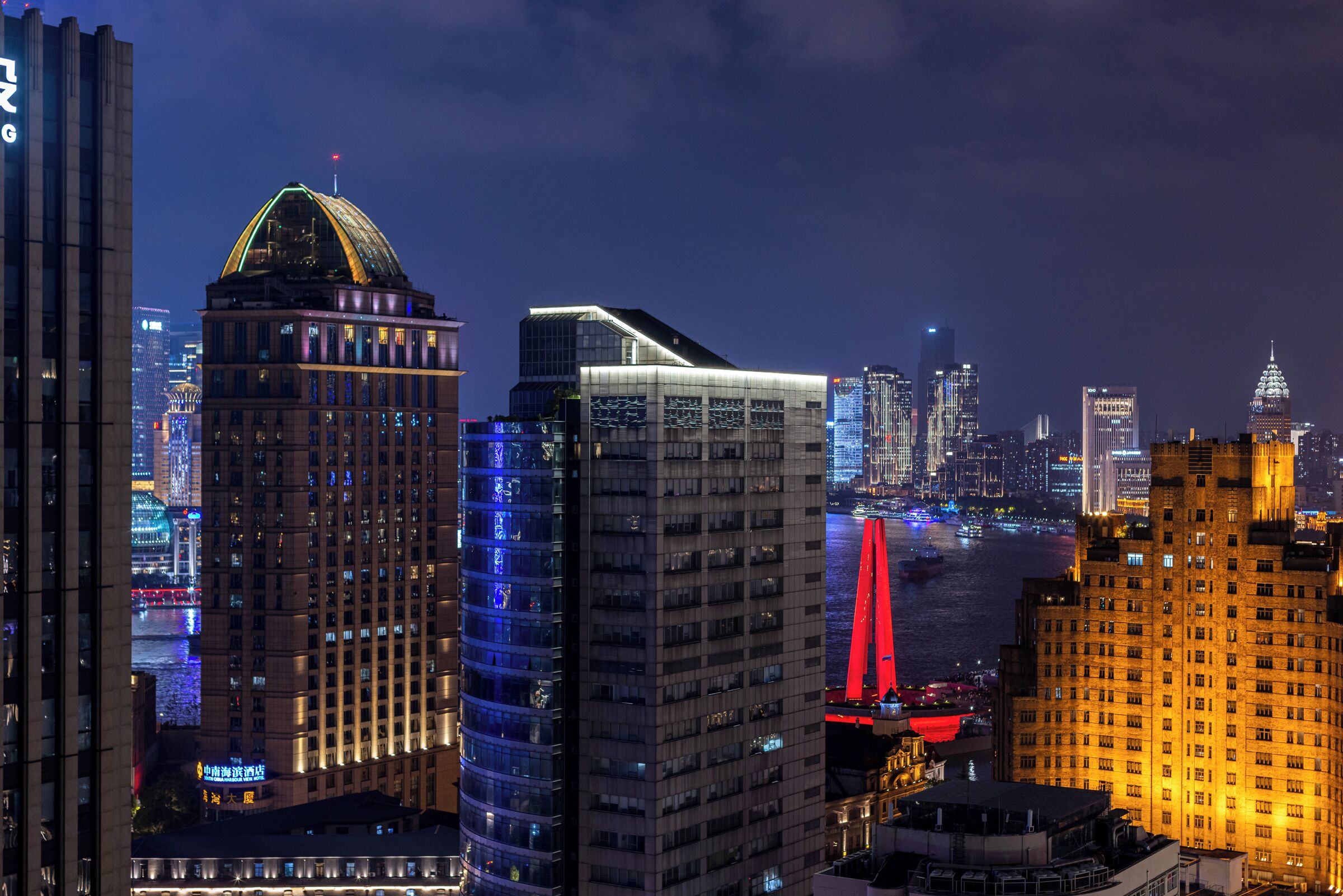 A cityscape at night with modern buildings, a prominent bridge, and a river.