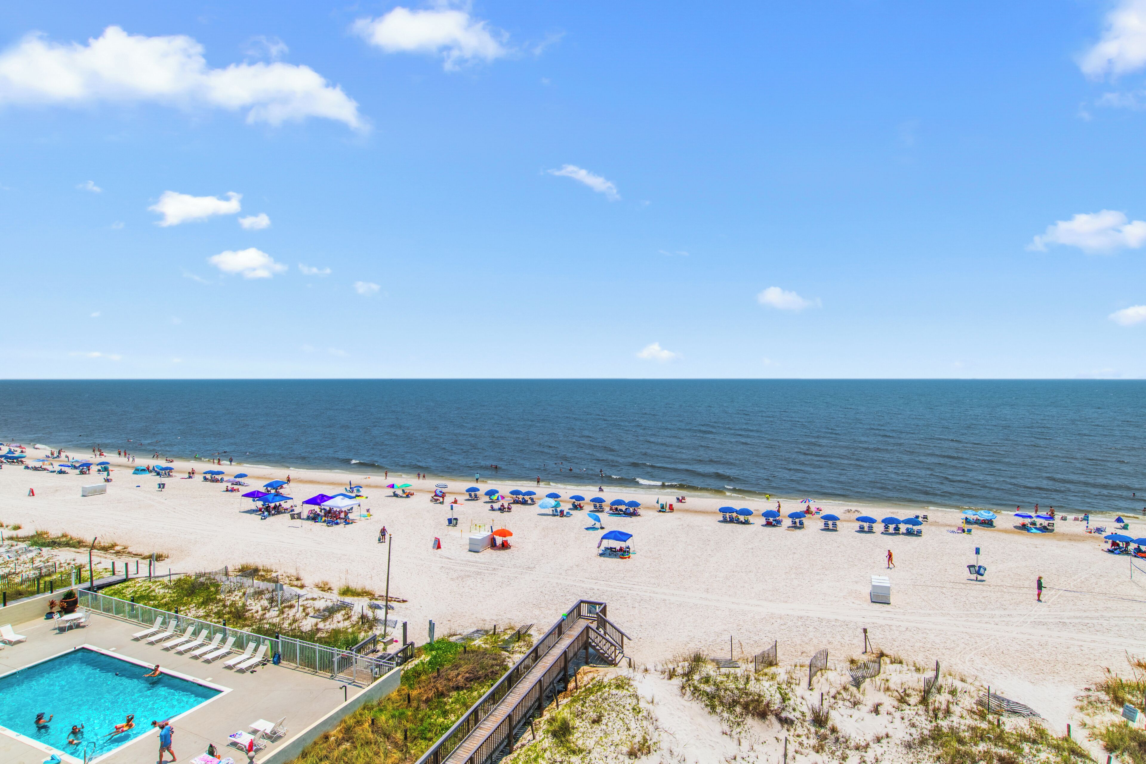 A beach with a pool area, beach umbrellas, and a wooden walkway.