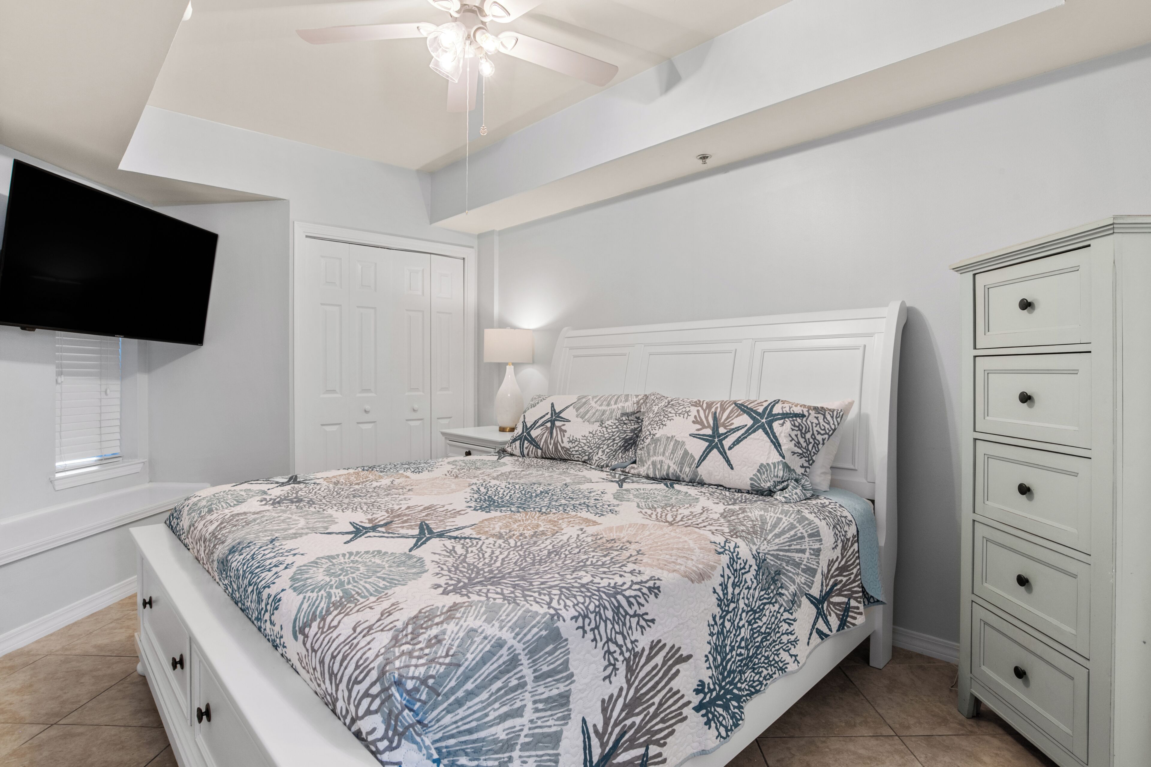 A bedroom with a bed, nightstands, a dresser, a television, and a ceiling fan.