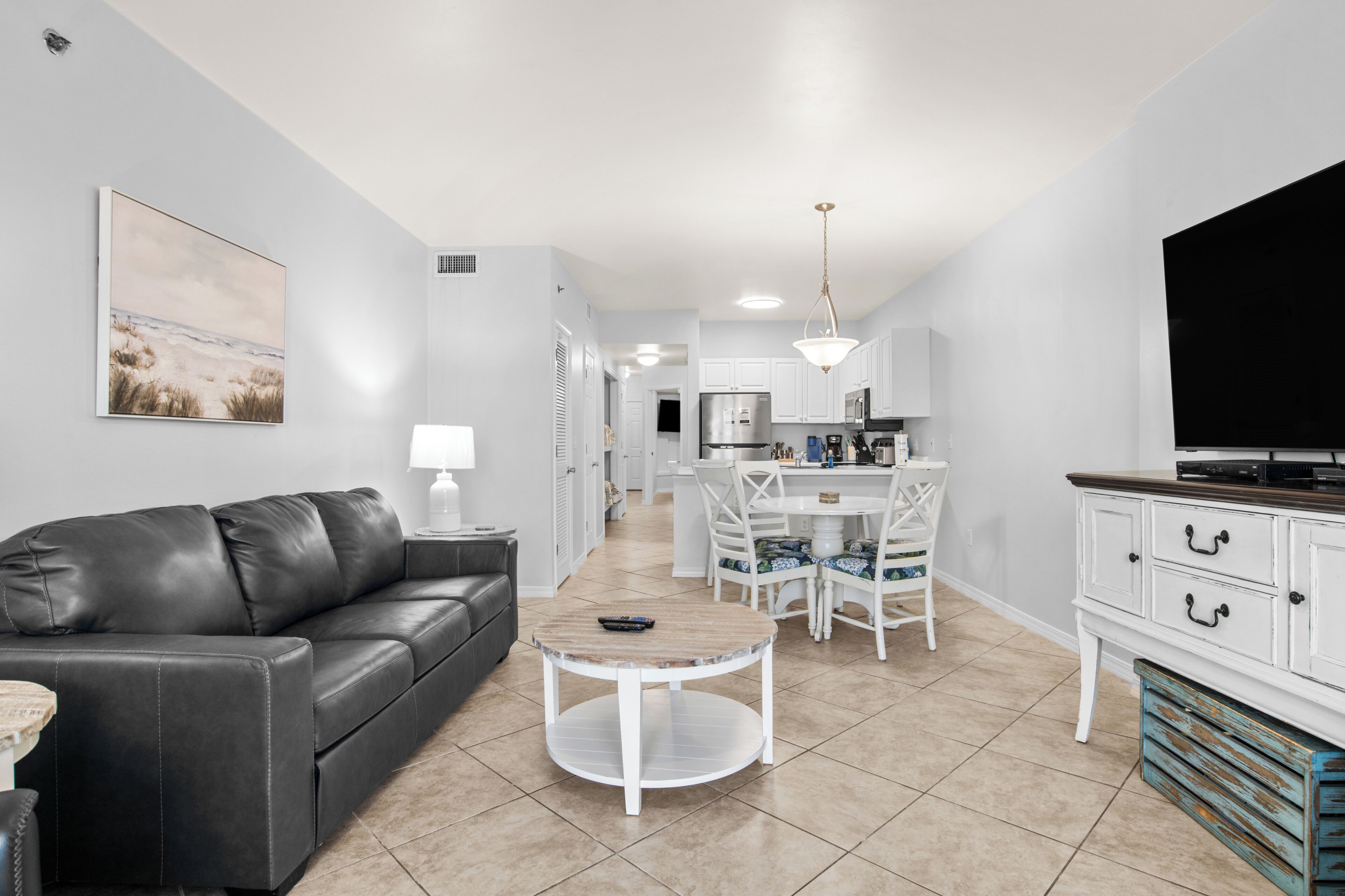 A modern living room with a black leather sofa, a round coffee table, and a dining area with white chairs and a white table.