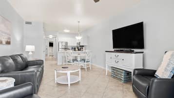 A modern living room with a sofa, a coffee table, a TV, and a dining area with chairs and a table.