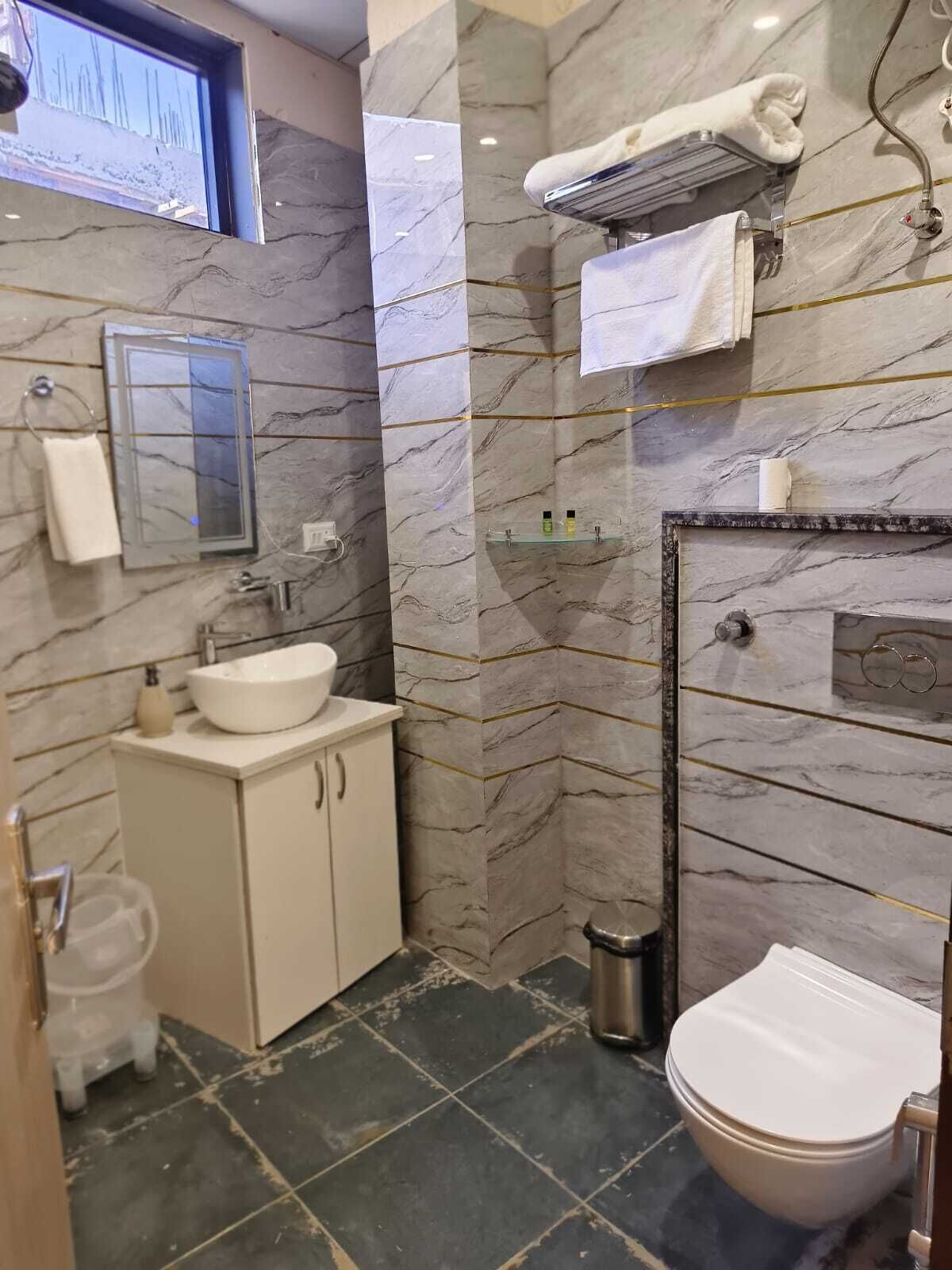 A bathroom with a white sink, mirror, and toilet. There is a towel rack and a small shelf with toiletries.