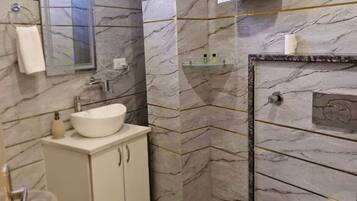 A bathroom with a white sink, mirror, and toilet. There is a towel rack and a small shelf with toiletries.