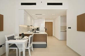 A modern kitchen with white cabinets, a wooden door, and a dining area with a table set for two. - Bloomfields 1BR in Binghatti Onyx  (Dubai)