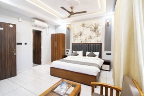 A hotel room with a bed, a desk, a chair, a ceiling fan, and a wall-mounted air conditioner.