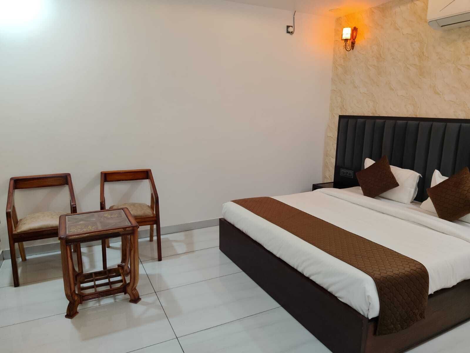 A hotel room with a bed, two chairs, a small table, and a wall-mounted light fixture.