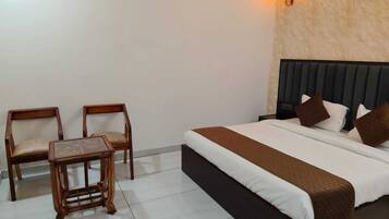 A hotel room with a bed, two chairs, a small table, and a wall-mounted light fixture.