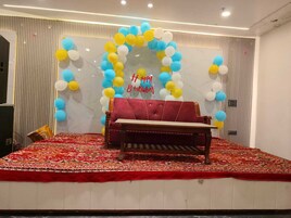 Una habitación con sofá rojo, alfombra estampada y una pared decorada con un arco de globos y un cartel que dice 'Happy Birthday'.