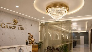 Een hotel receptie met een marmeren balie, een kroonluchter en een decoratieve Boeddha-beeld.