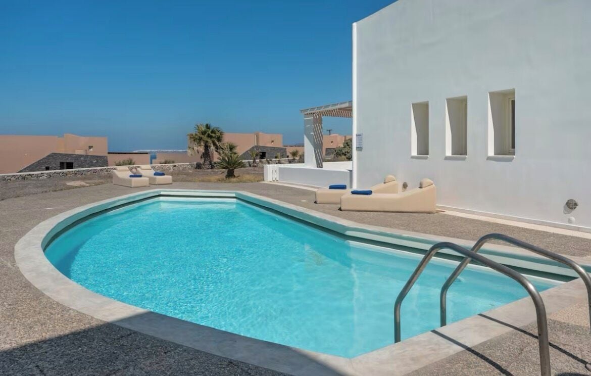 A swimming pool with a clear blue water, surrounded by a white wall and a few windows.
