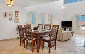 A dining area with a wooden table and chairs, a television, and artwork on the wall. - Solis Akrotiri Villa (Santorini)
