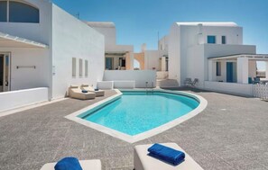 A modern pool area with lounge chairs and a clear blue pool, surrounded by white buildings. - Solis Akrotiri Villa (Santorini)