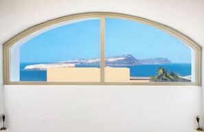 A window with a view of a coastal landscape, including a mountain and the sea. - Solis Akrotiri Villa (Santorini)