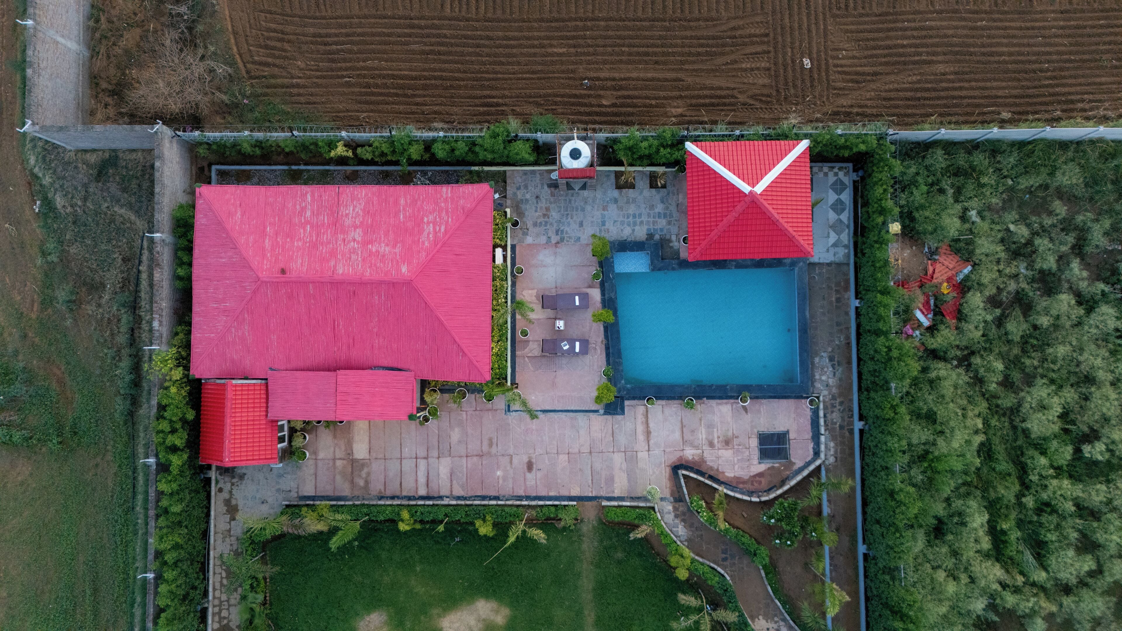 Vista aérea de una propiedad con piscina, dos construcciones con tejados rojos y un jardín ajardinado.