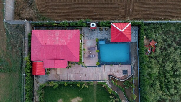 Vista aérea de una propiedad con piscina, dos construcciones con tejados rojos y un jardín ajardinado.