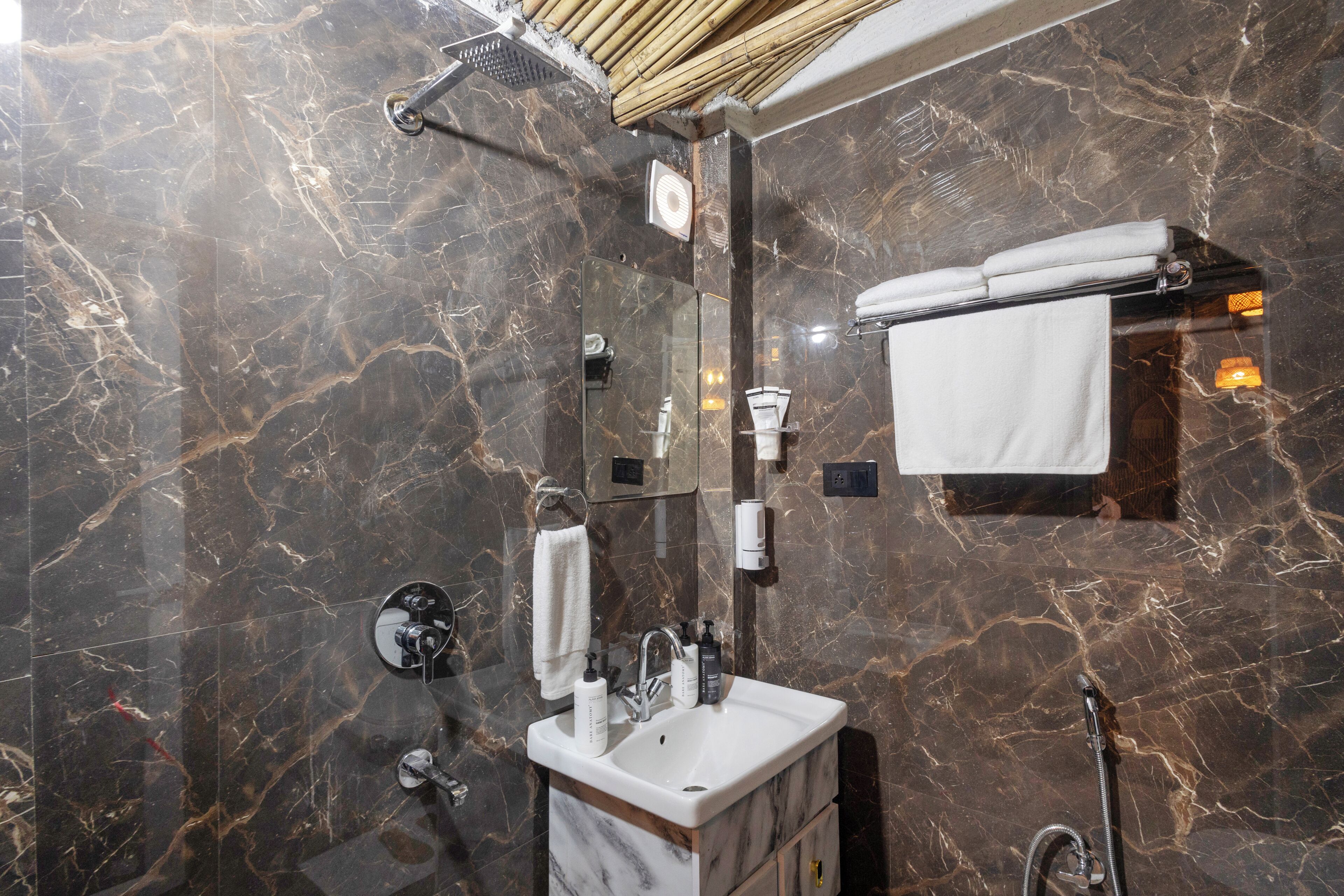 Un baño moderno con pared de mármol, ducha envuelta en vidrio, tocador con lavamanos y un perchero para toallas.