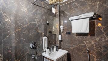 Un baño moderno con pared de mármol, ducha envuelta en vidrio, tocador con lavamanos y un perchero para toallas.