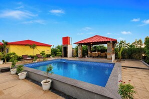 Una piscina con cubierta de baldosas, sillas de descanso y una zona de estar techada.