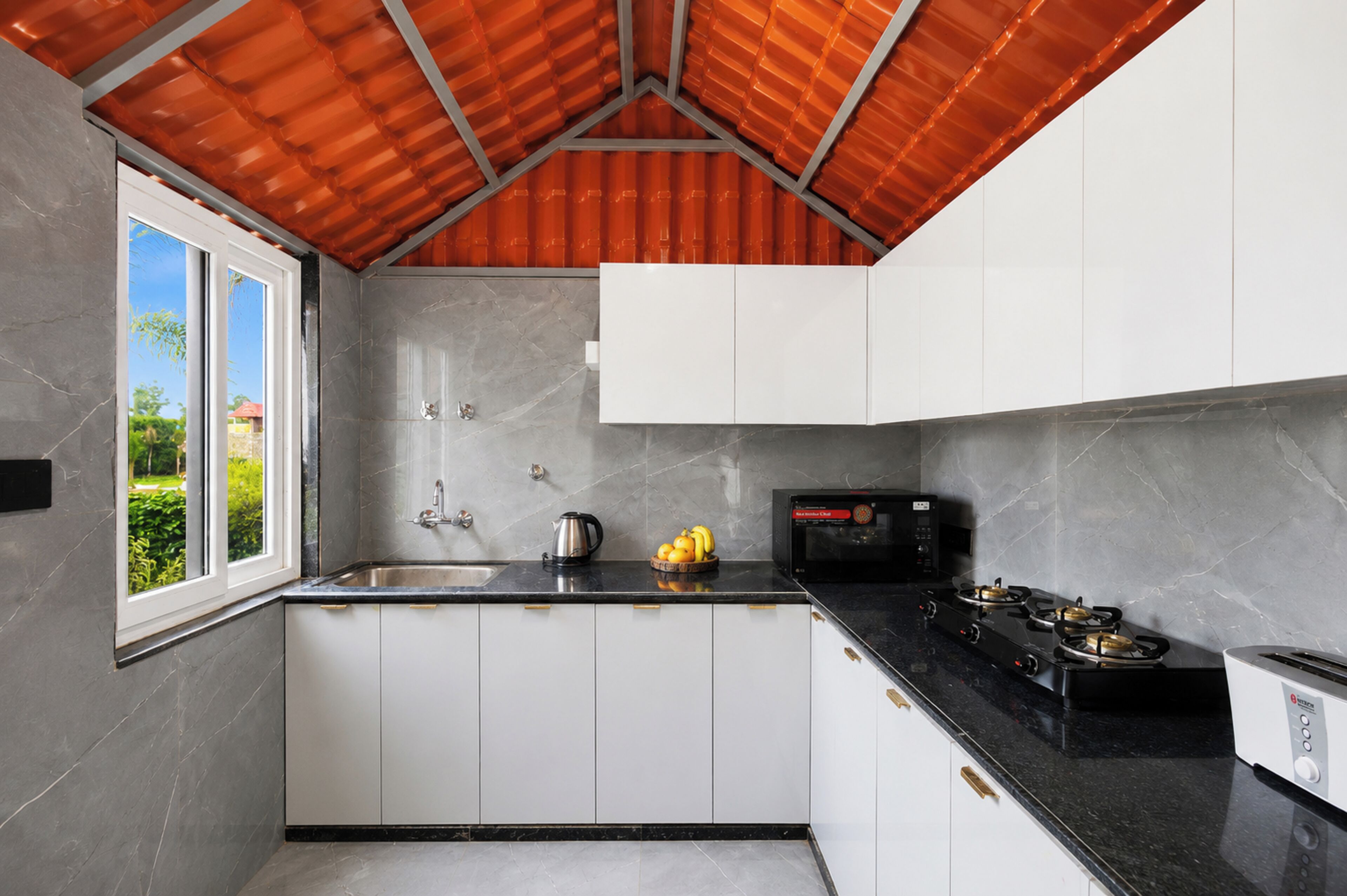 A modern kitchen with white cabinets, a black countertop, a gas stove, a microwave, and a window with a view of greenery.