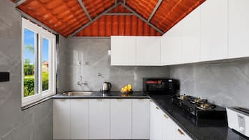 A modern kitchen with white cabinets, a black countertop, a gas stove, a microwave, and a window with a view of greenery.