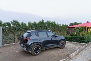 Un SUV negro estacionado en una entrada de casa, con un edificio de techo rojo al fondo.