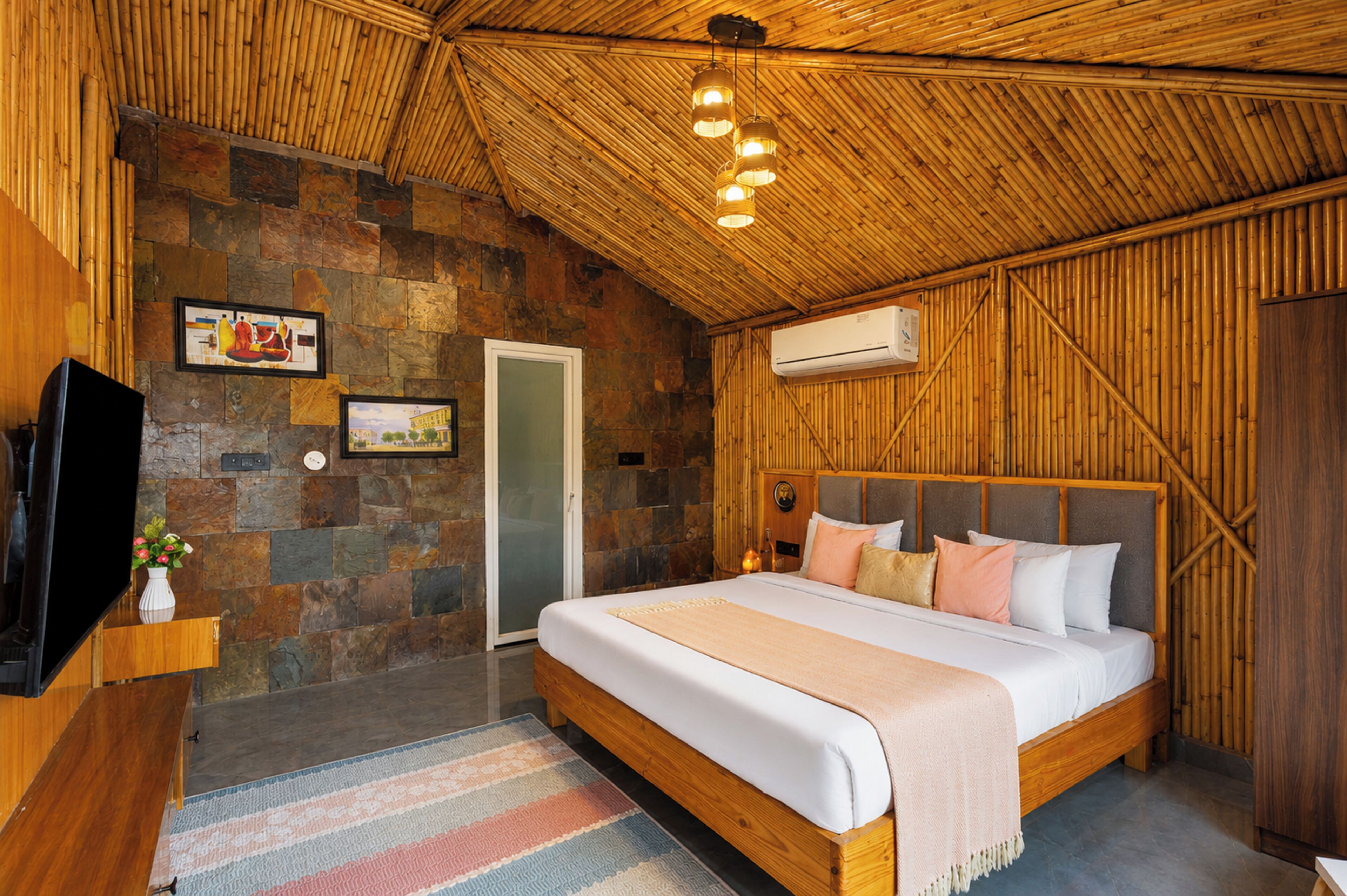 Un dormitorio con pared de piedra, cama con almohadas, televisor y unidad de aire acondicionado.