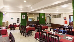 Een restaurant met meerdere tafels en stoelen, groene zuilen en ingelijste foto's aan de muren.