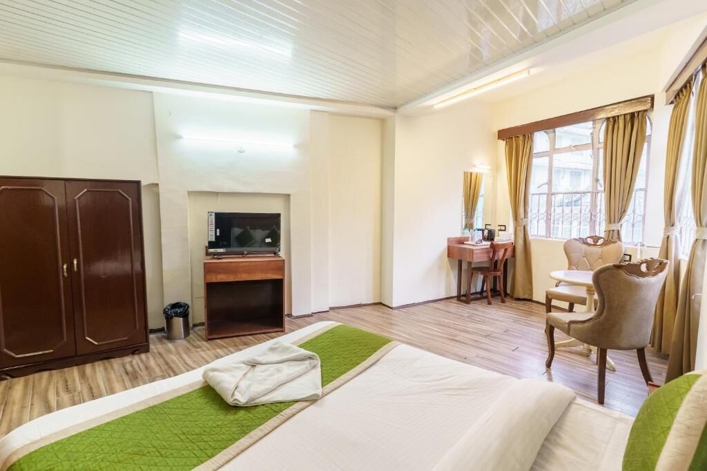 Habitación de hotel con cama, escritorio, computadora, televisor, una silla y ventana con cortinas.