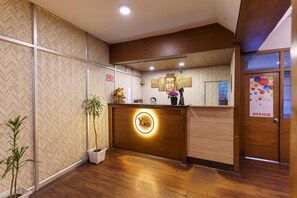 A reception desk with a logo, a potted plant, and a mirror reflecting the interior. - Hotel Yuma Darjeeling By Yagi group (Darjeeling)