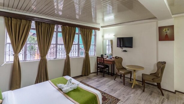 Hotelkamer met een bed, een bureau, twee stoelen, een televisie en een raam met gordijnen.