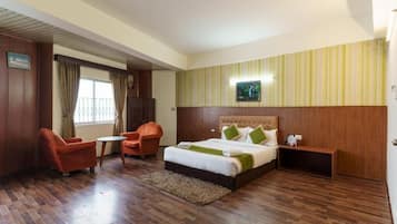 Habitación de hotel con cama, dos sillones, una mesita, una mesita de noche y una ventana con cortinas.