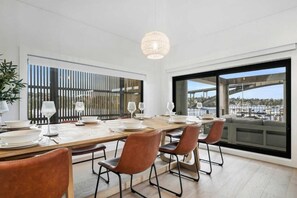 A dining area with a long table, multiple chairs, and a view of a harbor through large windows. - Unit 1 380 Drummoyne (Drummoyne)