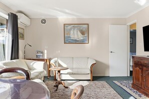 Ein Wohnzimmer mit einer Couch, einem kleinen runden Tisch, einem Schrank und einem Bild an der Wand.