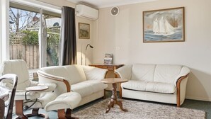 En stue med sofa, lænestole, et lille bord og et billede på væggen.