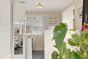 Ein Zimmer mit Heizkörper, einem Sessel, einem Schreibtisch und einem Fenster mit Spitzenvorhängen.