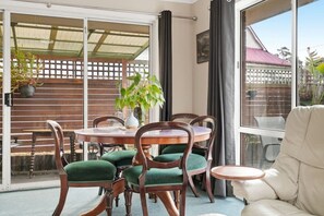 A room with a sliding glass door leading to a patio area, a round wooden table with chairs, and a potted plant. - King`s Corner Retreat (Sandy Bay)