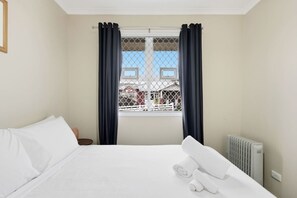 Ein Hotelzimmer mit Bett, einem fenster mit Vorhängen, einem Heizkörper und Blick auf ein Gebäude.